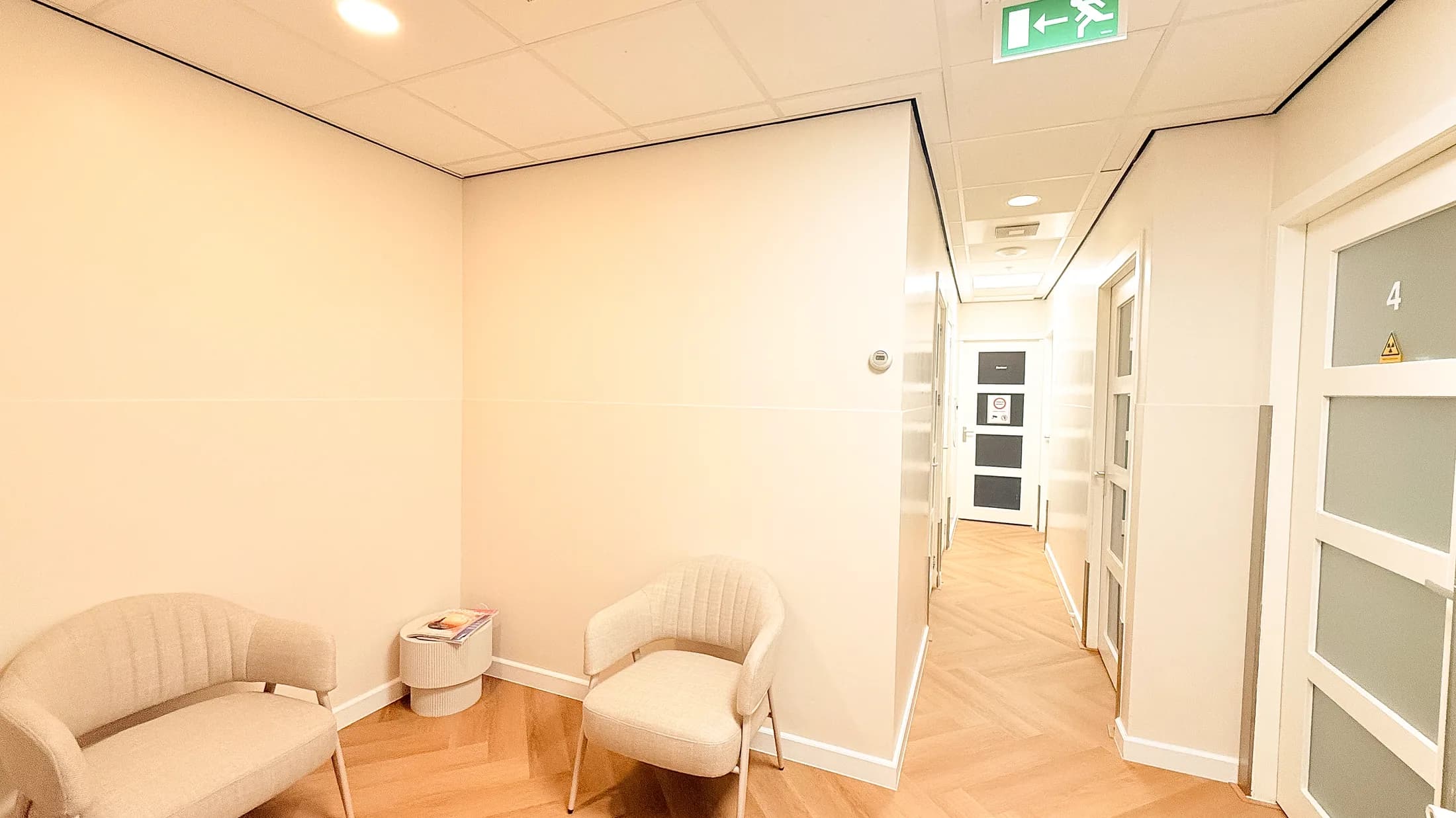 Rustige wachtruimte met twee fauteuils en een lichte gang naar de behandelkamers.