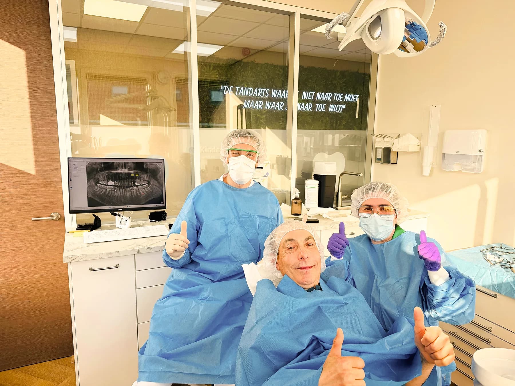 Twee teamleden en een tevreden patiënt steken lachend hun duim op na de behandeling.