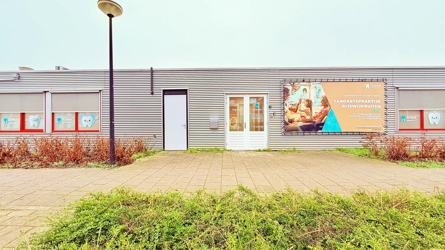 Buitenkant van de praktijk RijswijkBuiten met een groot spandoek naast de entree.